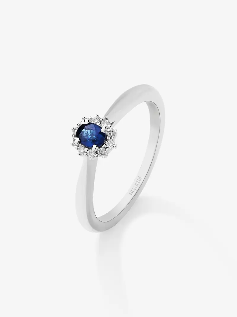 Anillo de oro blanco de 18K con zafiro azul central en talla oval de 0,20 cts y orla de diamantes en talla brillante