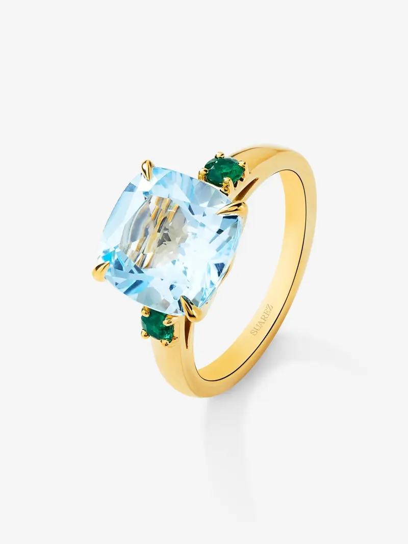Anillo tresillo de oro amarillo de 18K con topacio azul sky en talla cushion de 4,88 cts y 2 esmeraldas verdes en talla brillante